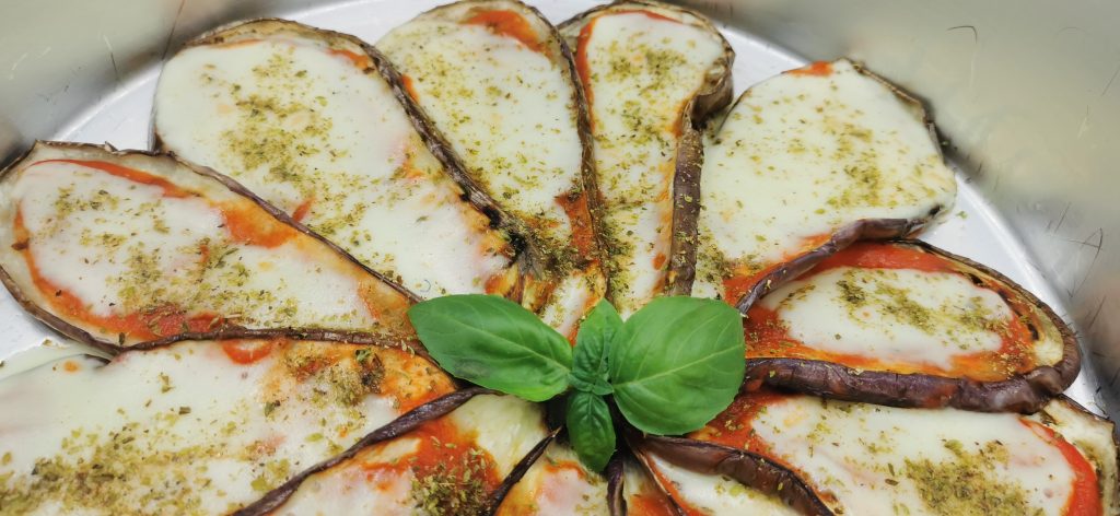 Rodajas de berenjena asada cubiertas de salsa roja y queso fundido dorado para Pizza de Berenjena
