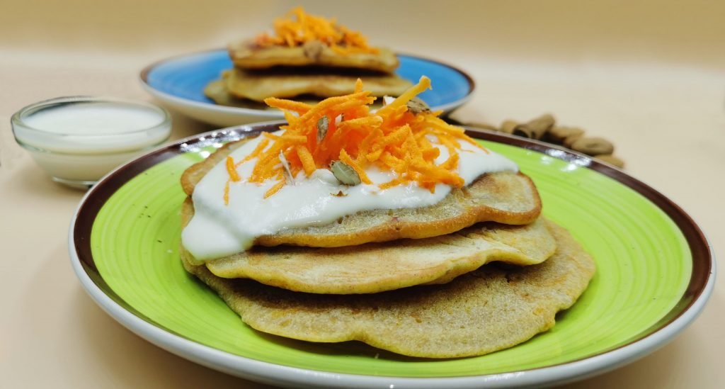 Tortitas doradas servidas con crema blanca de yogur y trocitos de almendra para Pancakes de Zanahoria