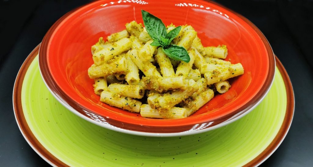 Pasta envuelta en salsa verde brillante y untuosa con trocitos de fruto seco para Pasta con Pesto