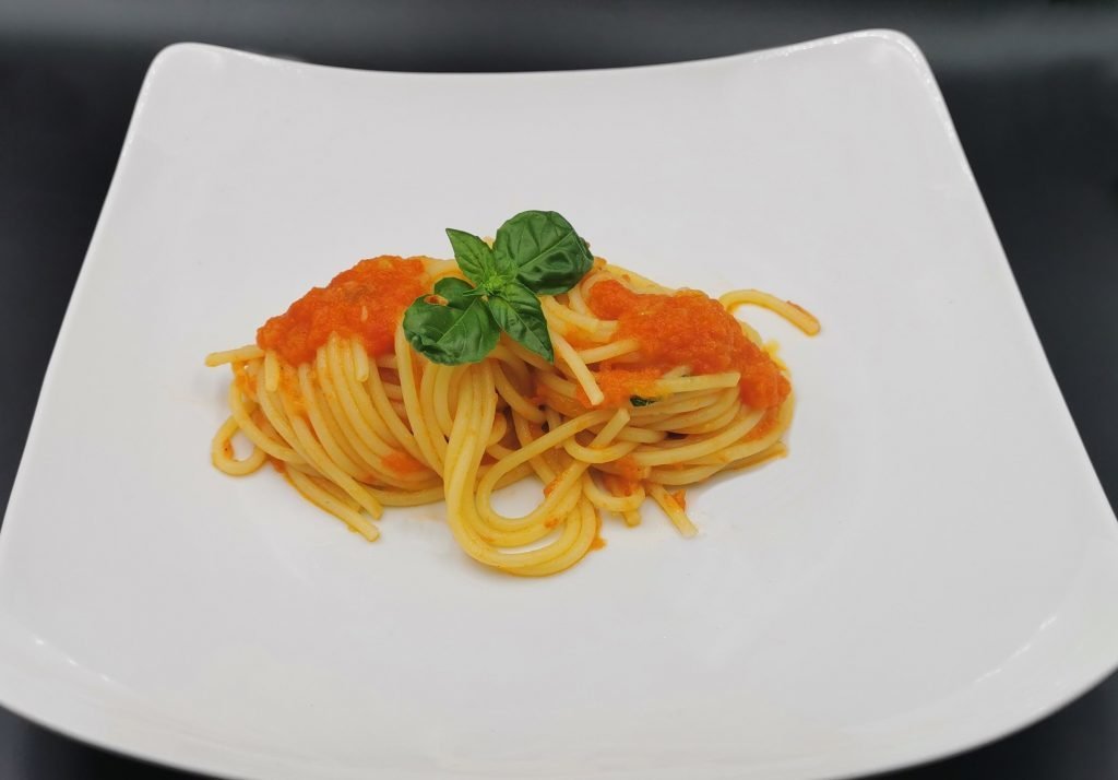 Nido de pasta larga bañado en salsa roja suave con hojas verdes frescas para Espaguetis con Tomate