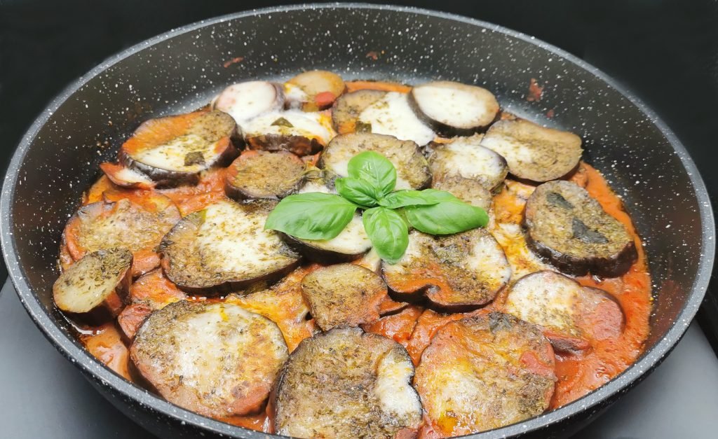 Capas de vegetales en salsa roja espesa con queso fundido y hierbas verdes para Berenjenas con Queso