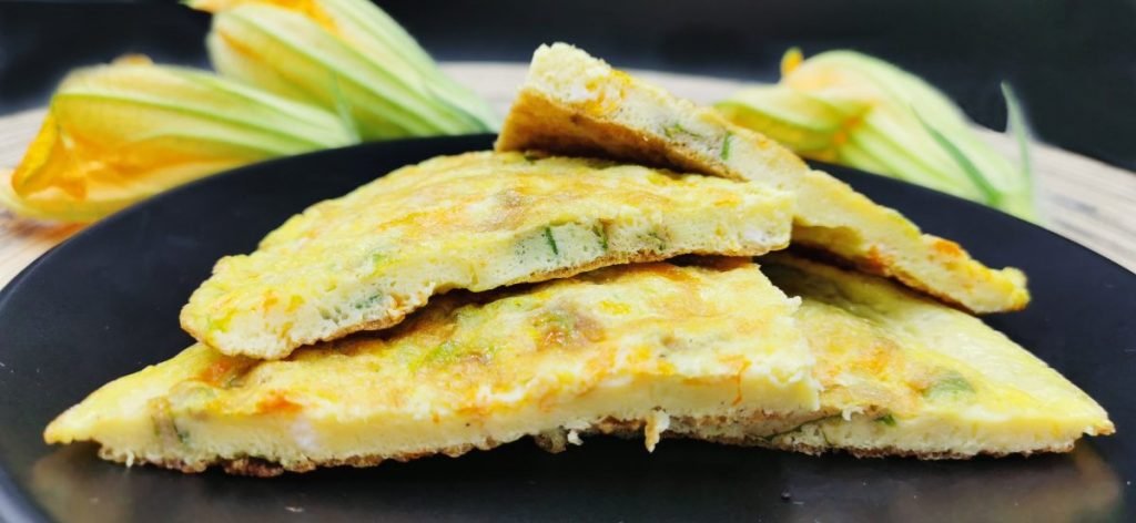 Tortilla esponjosa y dorada con flores de calabaza anaranjadas visibles para Omelet de Flores