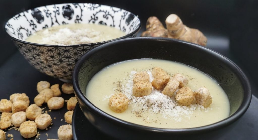 Sopa espesa y aterciopelada de tono marfil con queso espolvoreado para Crema de Papa con Topinambur