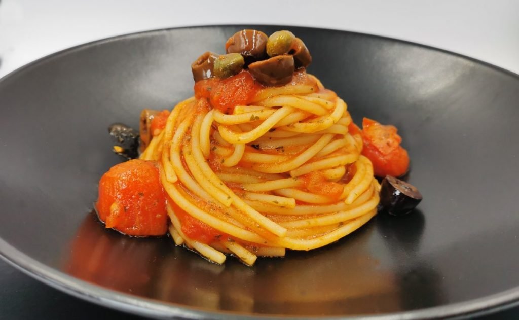 Pasta larga envuelta en salsa de tomate roja con aceitunas negras y alcaparras para Espaguetis a la Putanesca