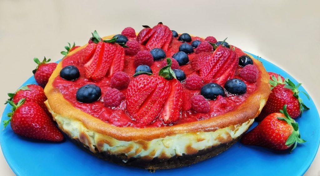 Pastel cremoso horneado con base dorada y cobertura brillante de fruta roja para Cheesecake de Fresas casero