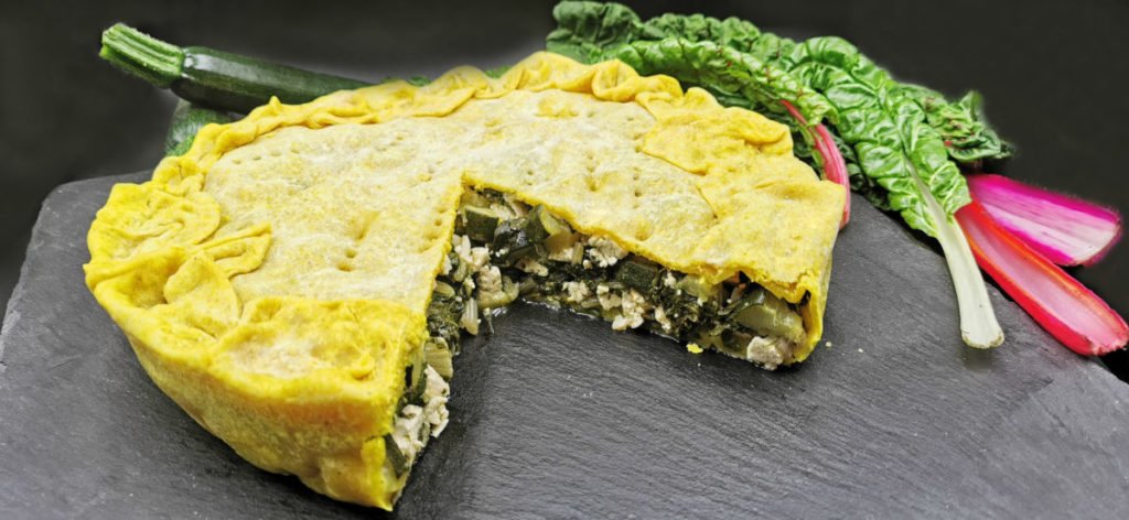 Tarta rústica dorada rellena de verduras verdes y trozos blancos de queso de soja para Pastel Salado de Acelgas