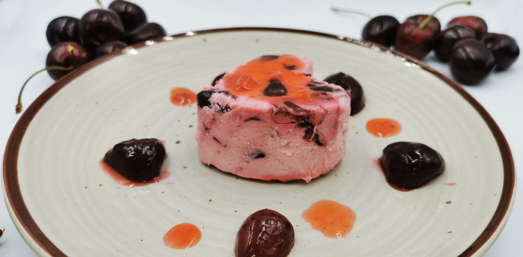 Postre moldeado suave y cremoso de color rosado con trocitos de fruta para Budín de Cerezas Vegano