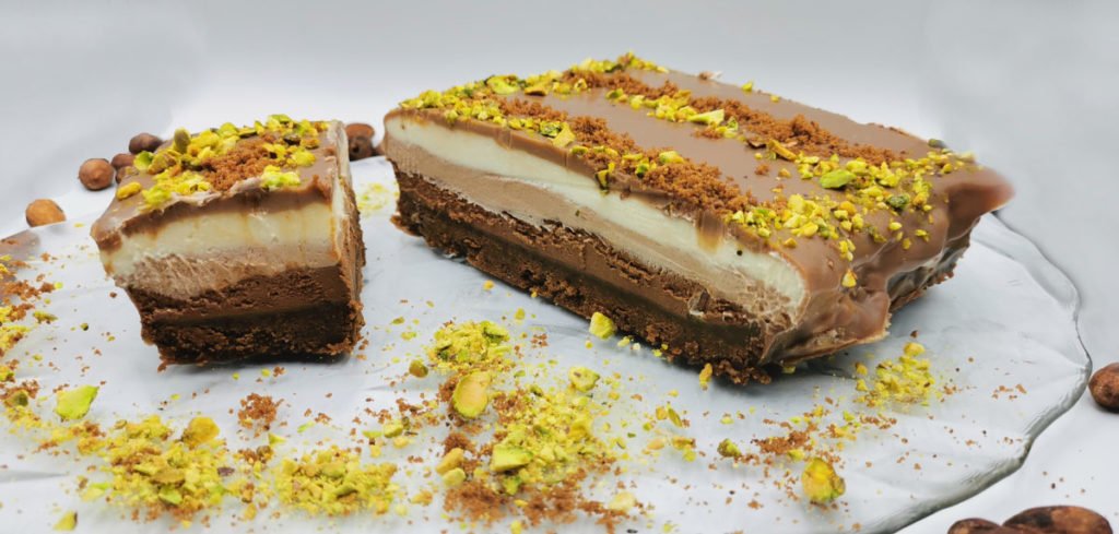 Pastel de tres capas cremosas con cobertura brillante y pistachos picados para Cheesecake Tres Chocolates